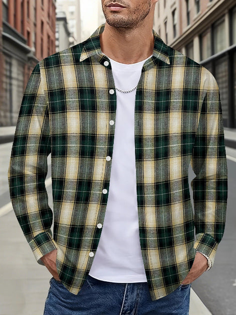 A man wearing a green and beige plaid button-down shirt over a white t-shirt and blue jeans, standing on a city street.