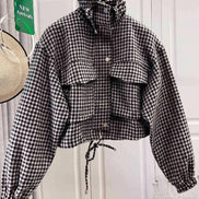 Black and white houndstooth utility jacket on a hanger, showing a raised drawcord collar, chest flap pockets, front snap buttons, elasticated cuffs and a tied drawcord hem