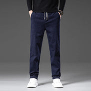 A person wearing dark navy drawstring jogger pants with a black sweater and white sneakers, shown from the chest down against a gray studio background.