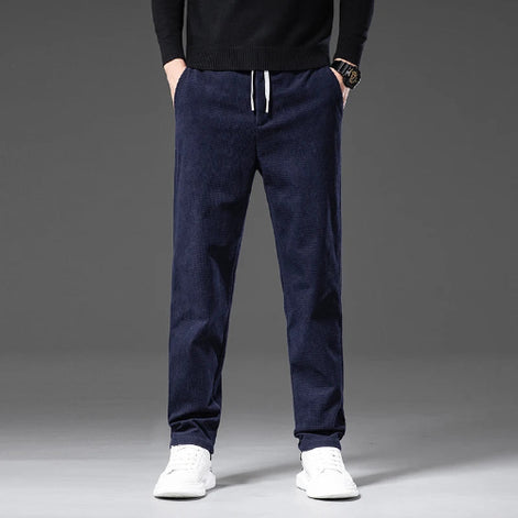A person wearing dark navy drawstring jogger pants with a black sweater and white sneakers, shown from the chest down against a gray studio background.