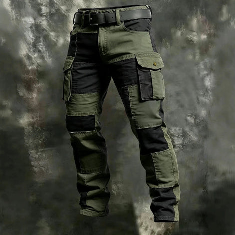 Olive green and black color-block cargo pants with flap thigh pockets and a black belt against a textured gray background.
