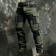 Olive green and black color-block cargo pants with flap thigh pockets and a black belt against a textured gray background.