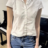 Person wearing a white short-sleeve shirt and blue jeans standing in front of a piano.