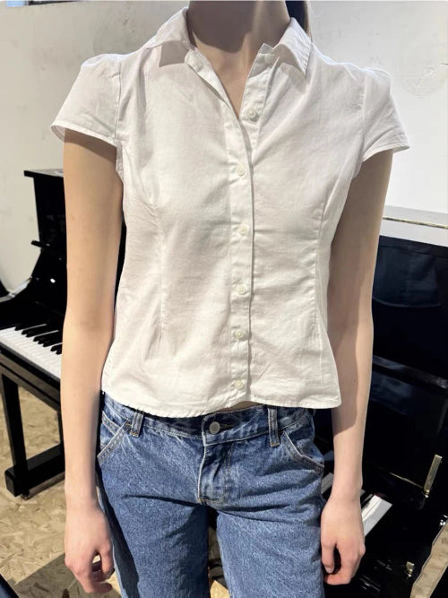 Person wearing a white short-sleeve shirt and blue jeans standing in front of a piano.