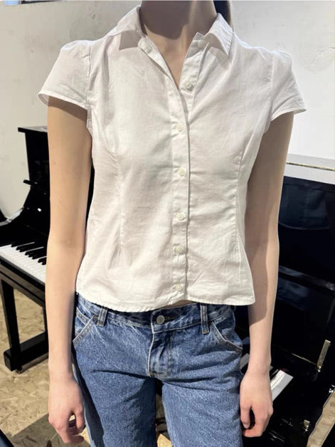 Person wearing a white short-sleeve shirt and blue jeans standing in front of a piano.