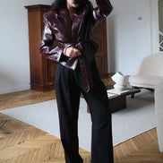 Woman taking a mirror photo wearing a glossy dark brown belted jacket with wide lapels and black wide-leg trousers