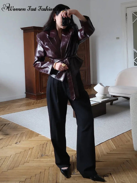 Woman taking a mirror photo wearing a glossy dark brown belted jacket with wide lapels and black wide-leg trousers