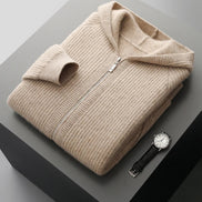 Folded beige sweater with a watch on a gray surface