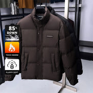 A dark brown puffer jacket displayed on a hanger stand in a retail setting, with a black puffer jacket behind it. Promotional graphic overlays on the left highlight features like 85% down, thick warm insulation, and fluffy soft texture.