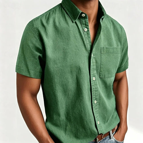 A man wearing a green short-sleeve button-up shirt with a chest pocket, paired with blue jeans and a brown leather belt, shown against a plain light background.