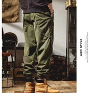 Rear-angle view of a model wearing olive green loose-fit cargo pants with curved seam detailing and gathered ankle cuffs, paired with tan boots.