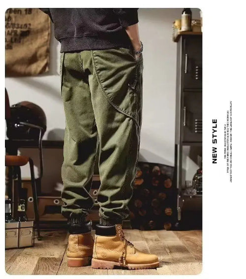 Rear-angle view of a model wearing olive green loose-fit cargo pants with curved seam detailing and gathered ankle cuffs, paired with tan boots.