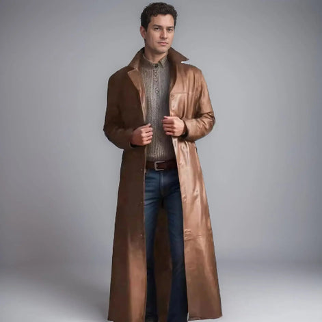 Man wearing a long brown coat over a sweater and jeans on a gray background