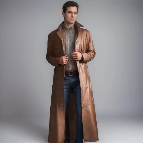 Man wearing a long brown coat over a sweater and jeans on a gray background