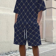A person wearing a navy blue short-sleeve t-shirt and matching shorts set, both featuring a repeating beige monogram pattern. 