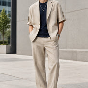 A men's light beige short-sleeve blazer styled over a black t-shirt and a silver necklace, presented on a white background 
