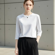 Person wearing a white long-sleeve shirt and black pants against a neutral background