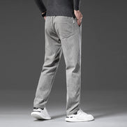 A person shown from the back wearing light gray textured pants, a dark gray sweater, and white sneakers against a dark gray studio background.