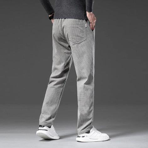 A person shown from the back wearing light gray textured pants, a dark gray sweater, and white sneakers against a dark gray studio background.