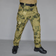 Front view of a model wearing tan and olive green camouflage cargo pants with a black belt and black lace-up boots against a gray background.