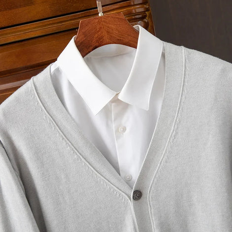 Gray cardigan over a white shirt on a wooden hanger against a dark background