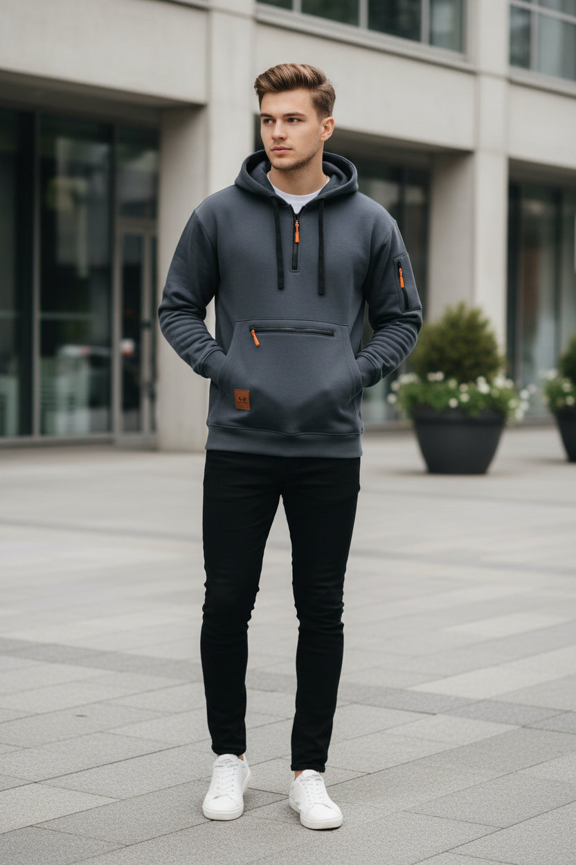 A dark gray pullover hoodie with a half-zip front, black drawstrings, a zippered front pocket, and a small brown brand patch on the lower left chest. The hoodie is shown against a plain white background.