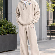 A man wearing a beige waffle-knit Reebok tracksuit, featuring a pullover hoodie with a drawstring hood and matching sweatpants, 