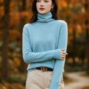 A woman wearing a fuzzy light blue turtleneck sweater, paired with beige trousers and a black belt with a gold buckle.