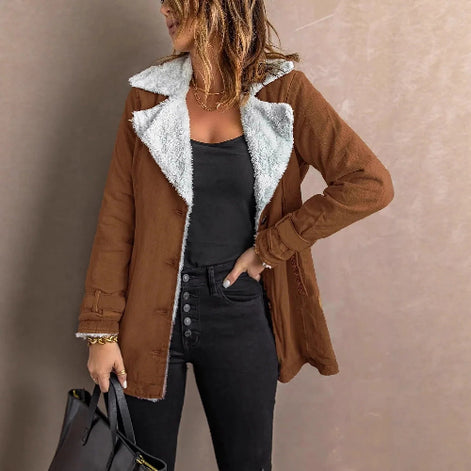 Woman wearing a brown jacket with white fleece-look lining, wide lapels and buckled cuffs over a black top and jeans⠋
