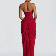 A woman modeling a strapless red evening gown from the back, showing a structured corset-style back and dramatic draped ruching, 
