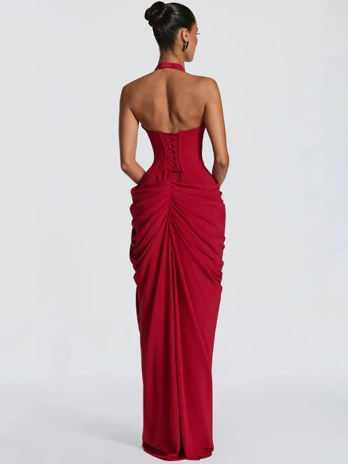 A woman modeling a strapless red evening gown from the back, showing a structured corset-style back and dramatic draped ruching, 