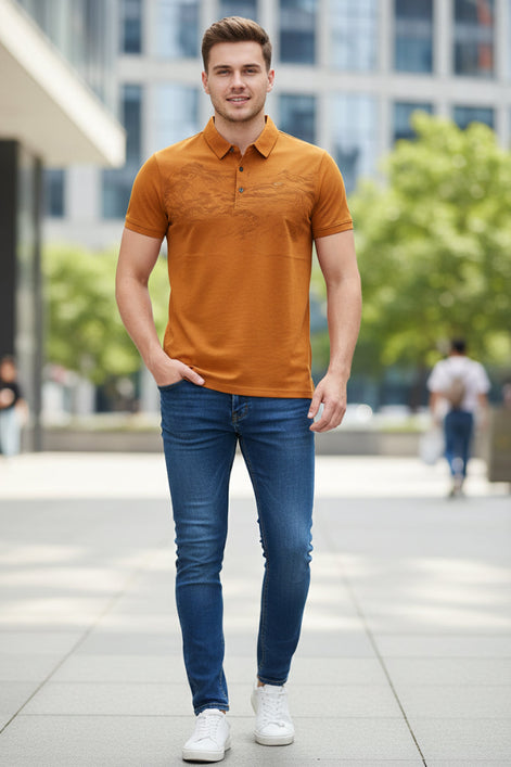 A close-up of a men's short-sleeve polo shirt in a warm orange-brown color, held by a hand to show its texture. The shirt features a subtle landscape pattern on the front and a small embroidered logo on the chest.