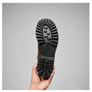 Person holding a black rubber sole of a shoe against a wooden floor.