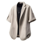 A light beige short-sleeve blazer with wide lapels and front patch pockets, styled open over a black t-shirt on a white background.