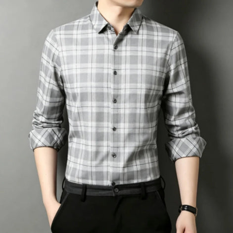 A man wearing a gray and white plaid long-sleeve button-down shirt with black trousers, shown from the chin down against a dark gray background.