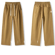 Front and back views of khaki straight-leg pants laid flat, showing an elastic waistband, white drawstring, slanted side pockets, and two back patch pockets.⠋