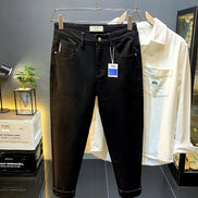 Black slim-fit jeans hanging on a metal rack, with a white button-up shirt behind them in a retail display setting.