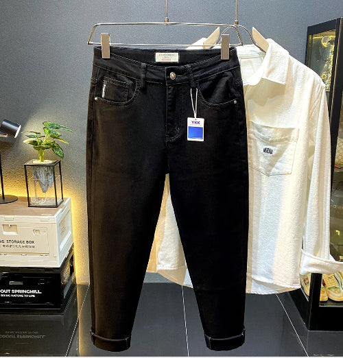 Black slim-fit jeans hanging on a metal rack, with a white button-up shirt behind them in a retail display setting.