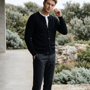 A black long-sleeve knit cardigan sweater hanging on a dark wooden hanger against a dark gray background.