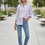 Woman wearing a light purple patterned shirt and blue jeans against a plain background