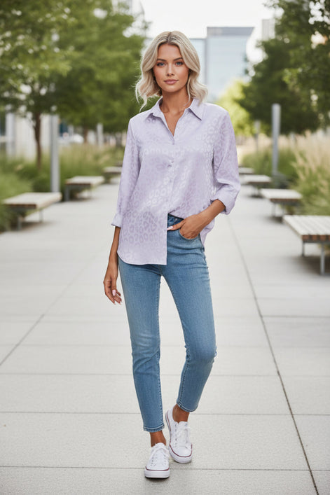 Woman wearing a light purple patterned shirt and blue jeans against a plain background