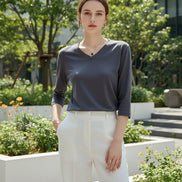 Person wearing a gray long-sleeve top sitting on a white surface with a neutral background