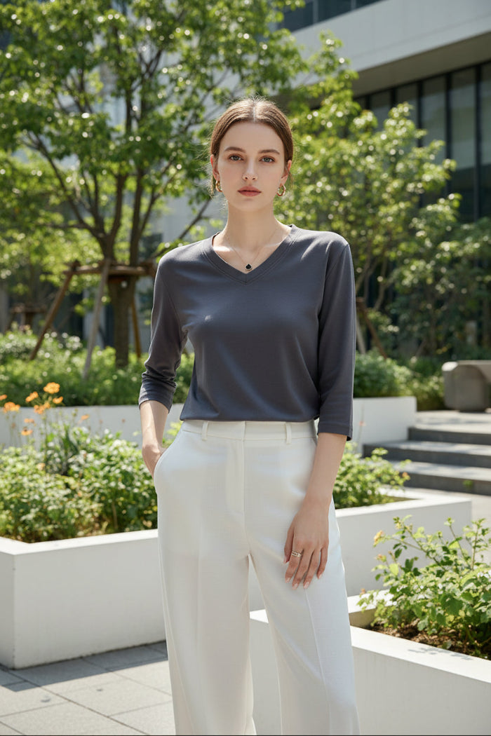 Person wearing a gray long-sleeve top sitting on a white surface with a neutral background
