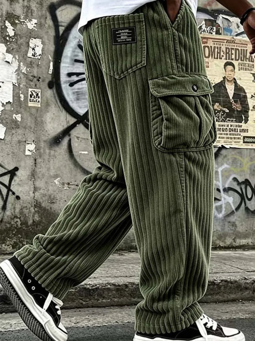 Olive green corduroy cargo pants worn by a model, featuring a ribbed corduroy texture, a large front flap pocket, and a black brand patch on the back pocket