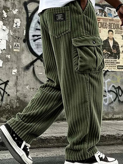 Olive green corduroy cargo pants worn by a model, featuring a ribbed corduroy texture, a large front flap pocket, and a black brand patch on the back pocket