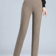 A model is shown from the waist down wearing slim-fit taupe pants and black heels, with a black long-sleeve top partially visible. A circular graphic overlay