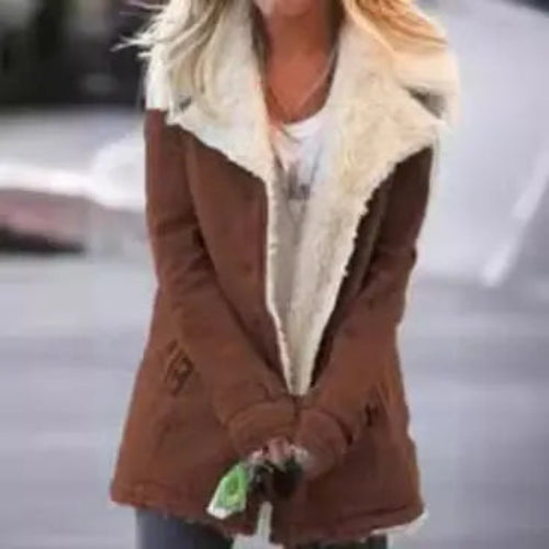 Woman outdoors wearing a brown coat with wide cream fleece-look lapels and front pockets, with her hands clasped in front