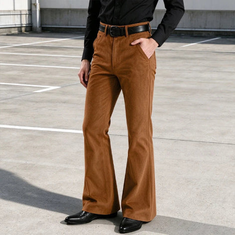 A person wearing brown wide-leg corduroy pants with a black belt, black long-sleeve shirt, and black shoes, standing in a concrete parking lot.