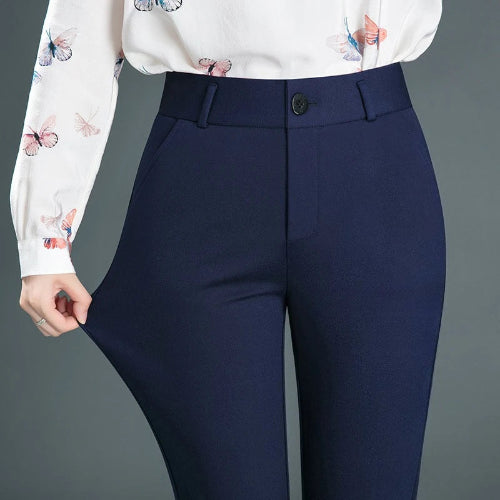A person wearing high-waisted navy blue trousers and a white long-sleeve blouse with butterfly prints, shown from the chest down against a plain gray studio background.