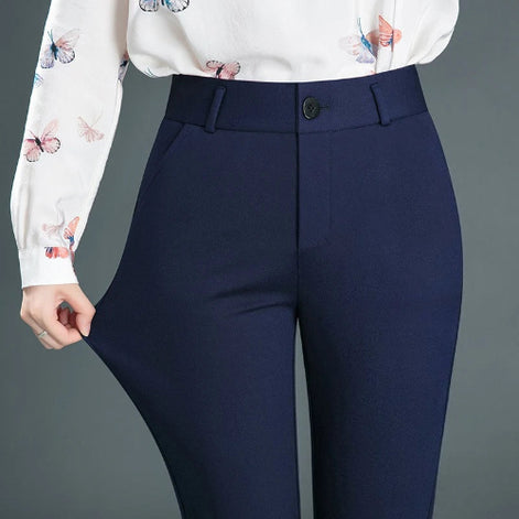 A person wearing high-waisted navy blue trousers and a white long-sleeve blouse with butterfly prints, shown from the chest down against a plain gray studio background.